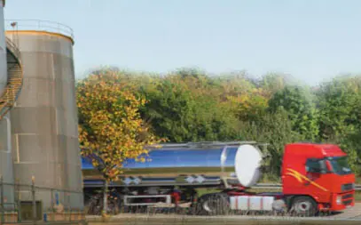 picture of a red 18 wheeler truck with a liquid carrying trailer parked next to a silo.